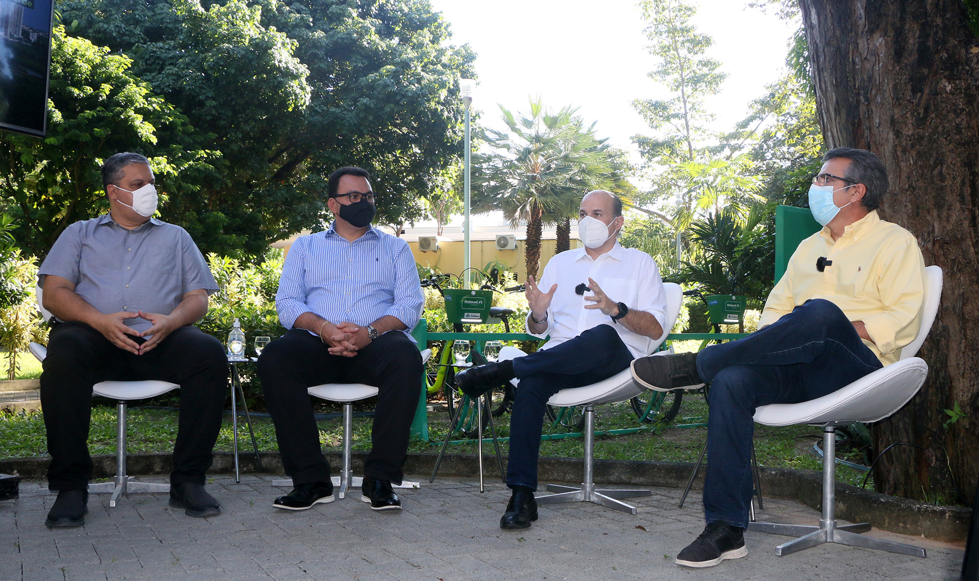 prefeito e três senhores usando máscara sentados em cadeiras posando para a foto com grande jardim ao fundo